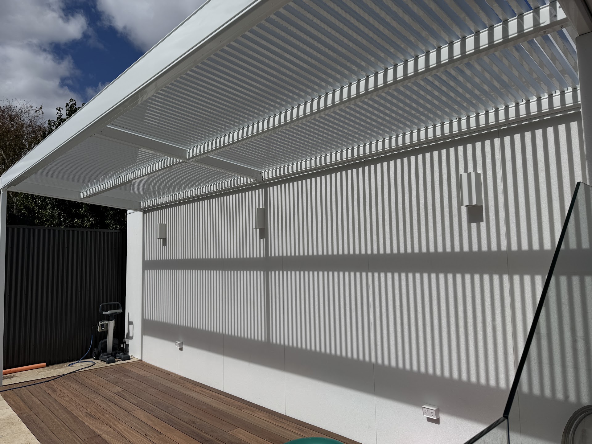 White pergola casting clean linear shadows over a timber deck